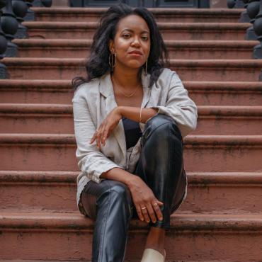 Whitney White, an African American woman, seated in front of a brown stone in Crown Heights, Brooklyn.